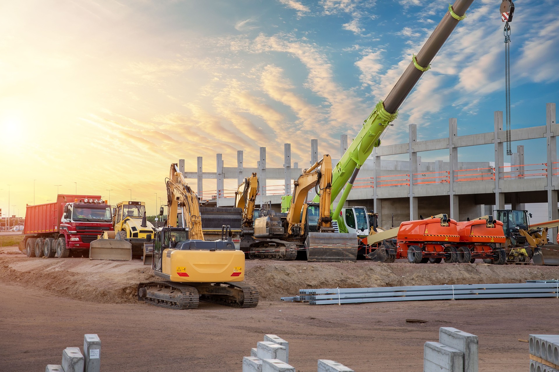 Many different multiclored colorful heavy industrial machinery equipment at construction site parking area against warehouse building city infrastructure development. Commercial vehicles rental sale